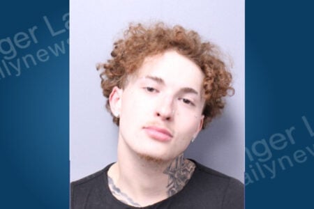 Young man with reddish-brown curly hair, facial piercings, and neck tattoos in a mugshot.