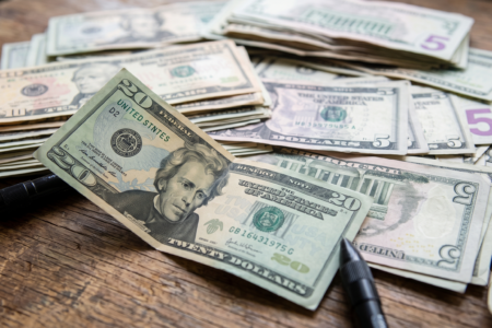 US twenty, ten, and five dollar bills spread across a worn wooden table, with a black pen nearby.