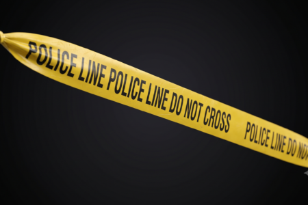 Yellow "POLICE LINE DO NOT CROSS" tape tied and stretched diagonally against a dark background.