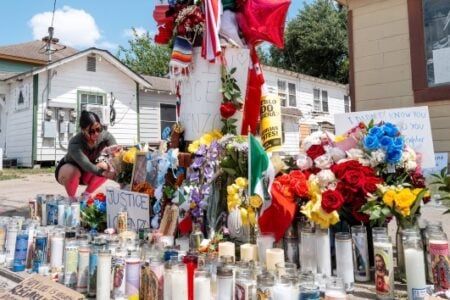Woman crouches, arranging flowers at a colorful street memorial with many candles and signs calling for justice.