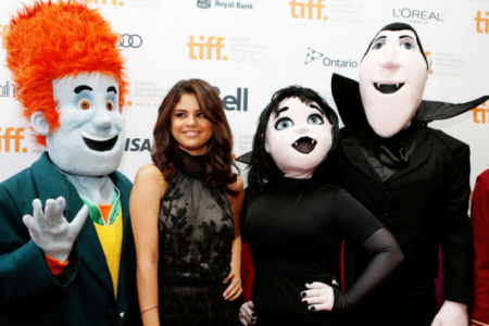 Selena Gomez poses smiling with Hotel Transylvania mascots Dracula and Mavis at the Toronto International Film Festival.