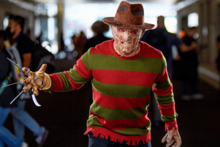 Freddy Krueger in full costume with burnt face mask and blade glove reaches out in a busy corridor.