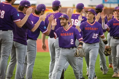Smiling Hobart College baseball players walk off the field, giving high-fives.