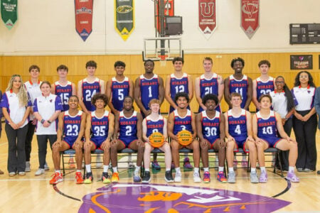 Hobart men's basketball team, coaches, and staff pose for a group photo on a gymnasium court.