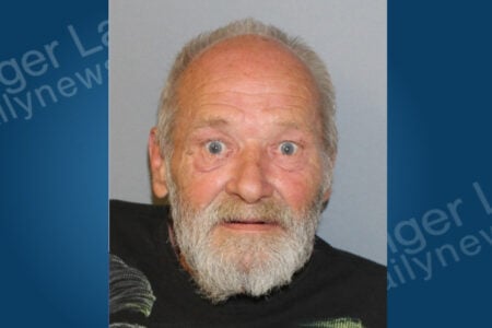 Elderly man with gray hair and beard, eyes wide and mouth slightly open, stares forward against a plain background.