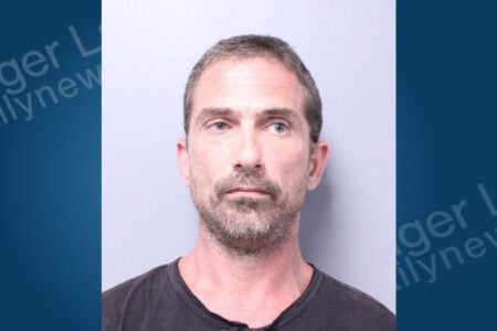 Mugshot of a man with short brown-grey hair and beard, wearing a dark shirt, looking forward against a light background.