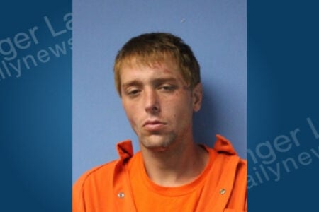 Mugshot of a young man with blond hair and facial scratches, wearing an orange jumpsuit against a blue background.