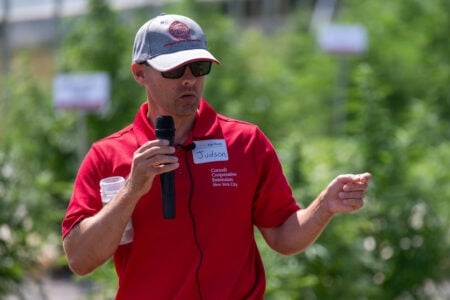 Judson, from Cornell AgriTech and Cooperative Extension, speaks into a mic, gesturing amidst green crops.