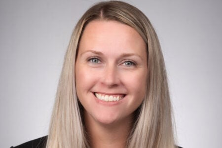 Headshot of a smiling woman with long blonde hair and blue eyes against a light grey backdrop.
