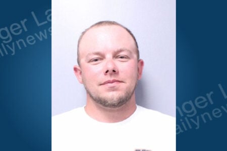 Man with short hair and a beard, wearing a white shirt, faces the camera in a booking photo.