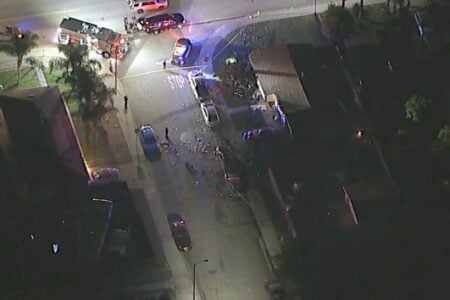 Aerial view of a residential street at night with a fire truck, police cars, and crash debris near a home.