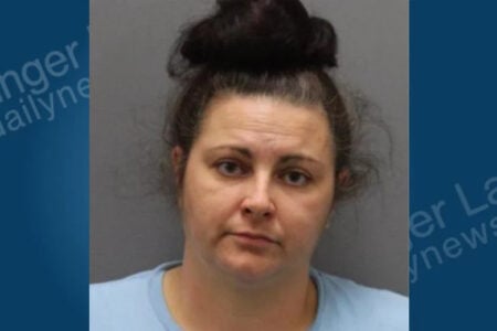 Mugshot of a woman with dark hair in a bun, wearing a light blue shirt, looking directly at the camera.