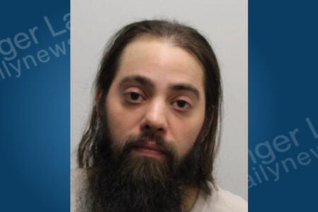 Man with long dark hair and a full dark beard stares directly into the camera for a mugshot.