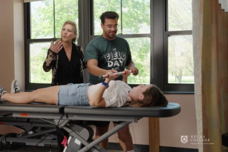 Keuka College OT instructor observes a student assisting another student with an exercise in a therapy lab.