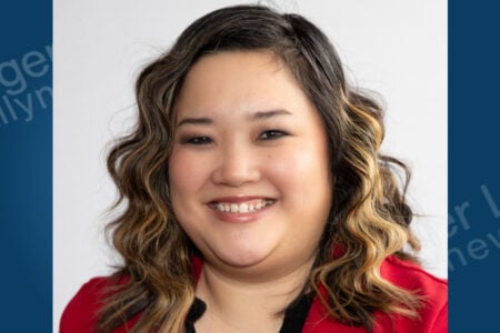 Headshot of a smiling woman with wavy brown hair in a red jacket against a white background.