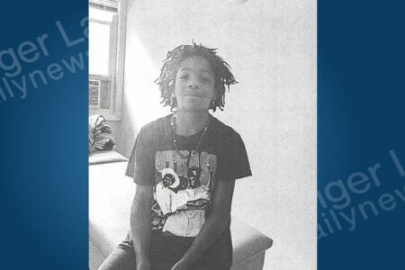 Young person with dreadlocks, Outkast t-shirt, sits smiling in a black and white room with a window.