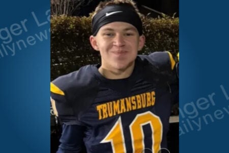 Young man in a Trumansburg #10 football jersey and Nike headband smiles outdoors with foliage in the background.