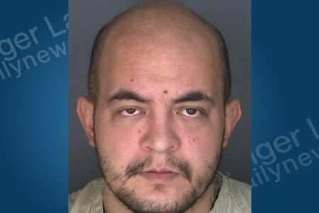 Bald man with mustache and goatee, wearing a light shirt, poses for a mugshot against a plain background.