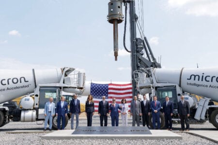 Officials and executives mark Micron's 'First Concrete Progress' in Central NY, flanked by concrete trucks and a US flag.