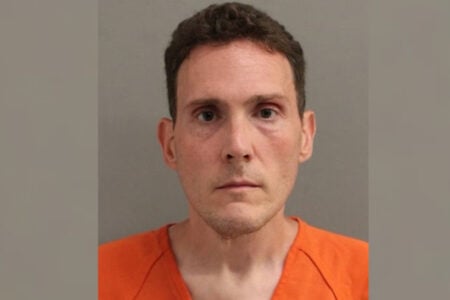 Mugshot of a man with short brown hair, wearing an orange shirt, looking forward.