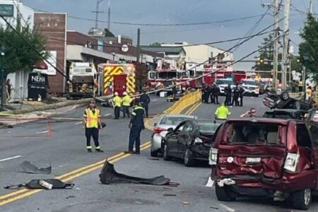 Emergency responders at a multi-vehicle crash scene with a fallen utility pole and overturned car on a city street.