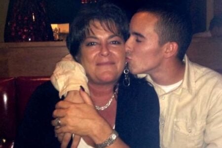 A young man kisses the cheek of a smiling woman, who has her arm around him, in a restaurant booth.