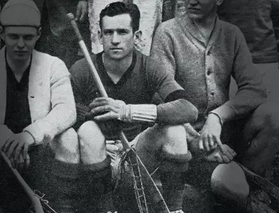 Three male lacrosse players from the early 20th century sit on outdoor steps with their sticks.