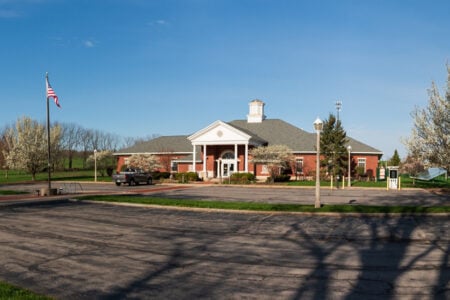 Red brick building with white columns, cupola, and an American flag, surrounded by blossoming trees and solar panels on a clear day.