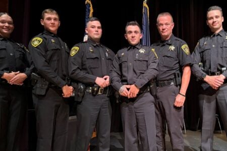 A group of six Ontario County Sheriff's deputies in uniform stand on a stage.
