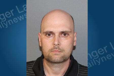 Mugshot of a bald man with light facial hair, wearing a striped polo shirt, looking straight ahead.