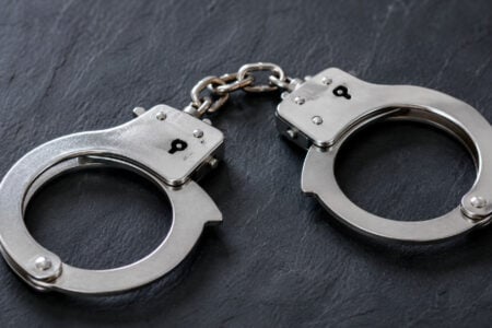 Silver metal handcuffs lie on a dark gray slate surface.