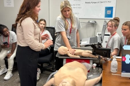 St. John Fisher University instructor supervises students practicing CPR on infant and adult mannequins in a medical lab.