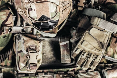 Military camouflage tactical vest, multiple attached pouches, and tan tactical gloves laid flat.