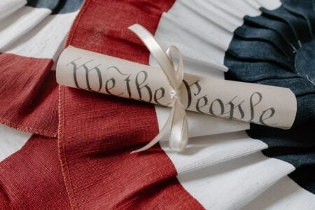 A rolled scroll inscribed "We the People" with a decorative ribbon, set on red, white, and blue pleated fabric.