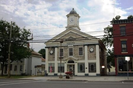 Phelps Town Hall, a two-story stone building with classical columns and a clock tower, stands on a street in Phelps, NY.