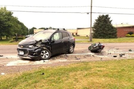 Damaged black Chevrolet SUV and motorcycle on a roadside with debris from a crash, near the Auburn Concrete building.